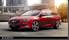 A vibrant red Holden Commodore station wagon parked on a paved city street, viewed from the front-three-quarter angle. Modern buildings are in the background.