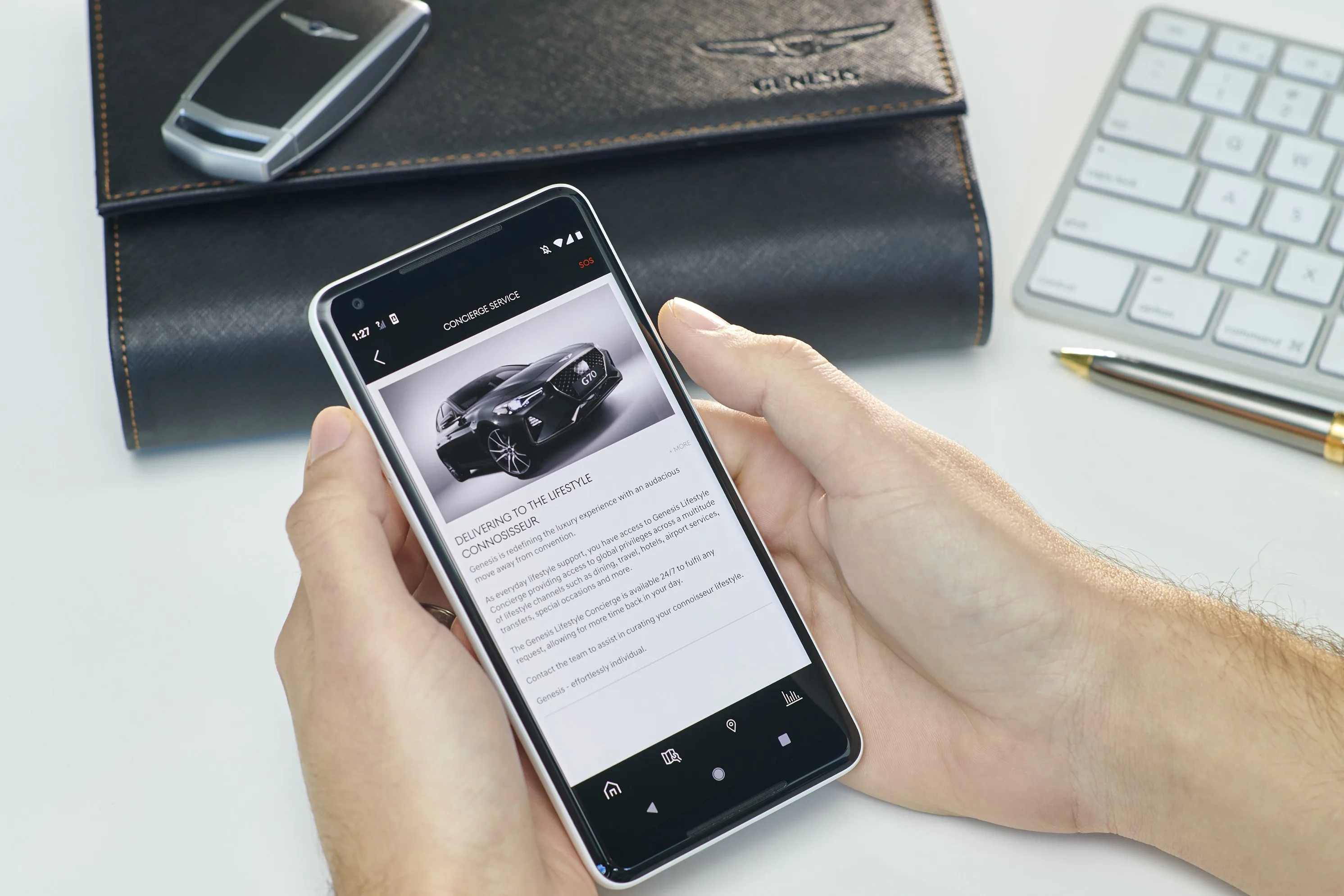 Hands hold a smartphone displaying the Genesis Connected Services app with a black Genesis car image.