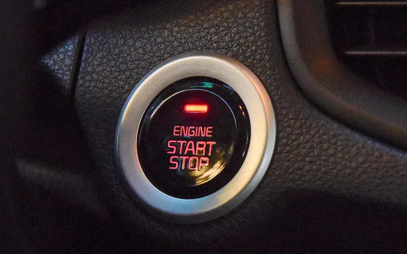 Close-up of a glowing red 'ENGINE START STOP' button with a silver trim on a black car dashboard.