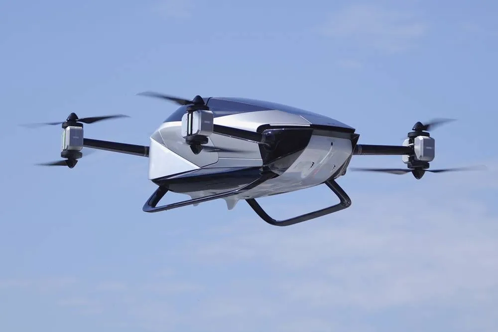 A sleek silver and black XPENG X2 personal electric copter hovers in a clear blue sky.
