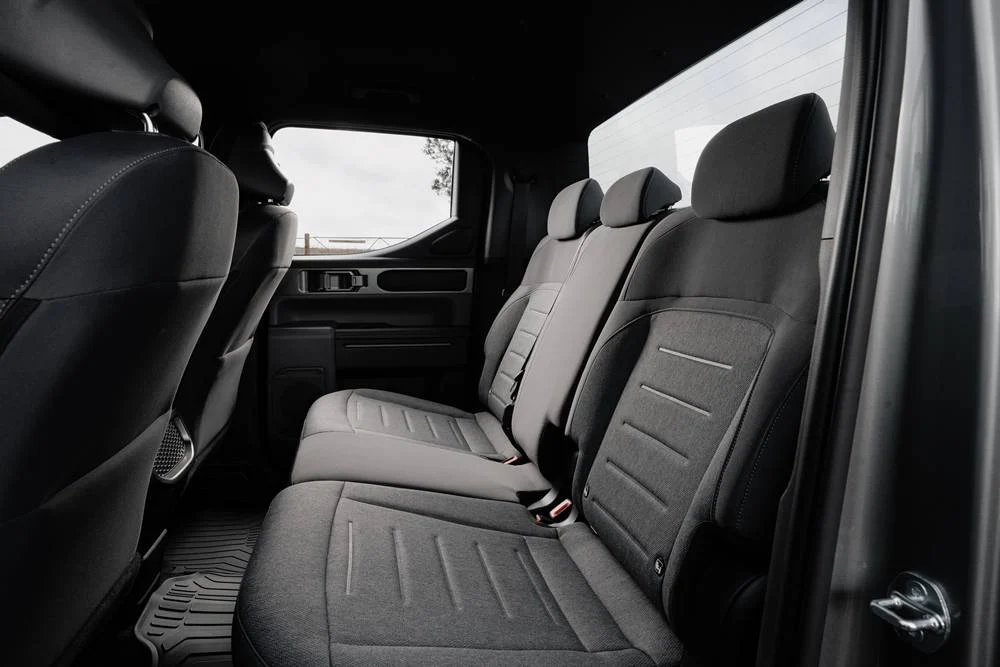 Rear interior view of a car, showing three dark grey fabric seats with subtle stripe patterns.