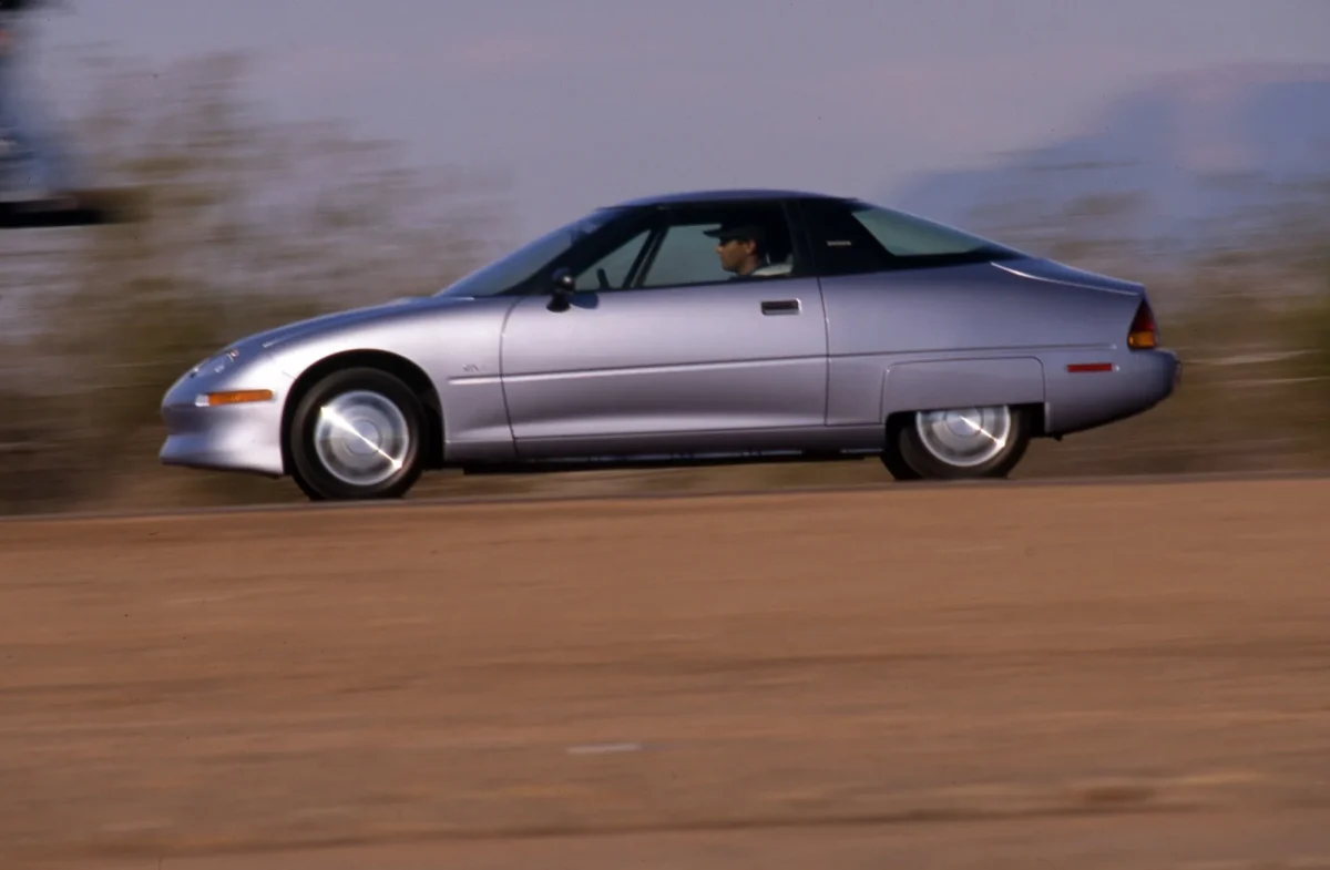 GM EV1 silver side profile driving at speed on desert road with motion blur
