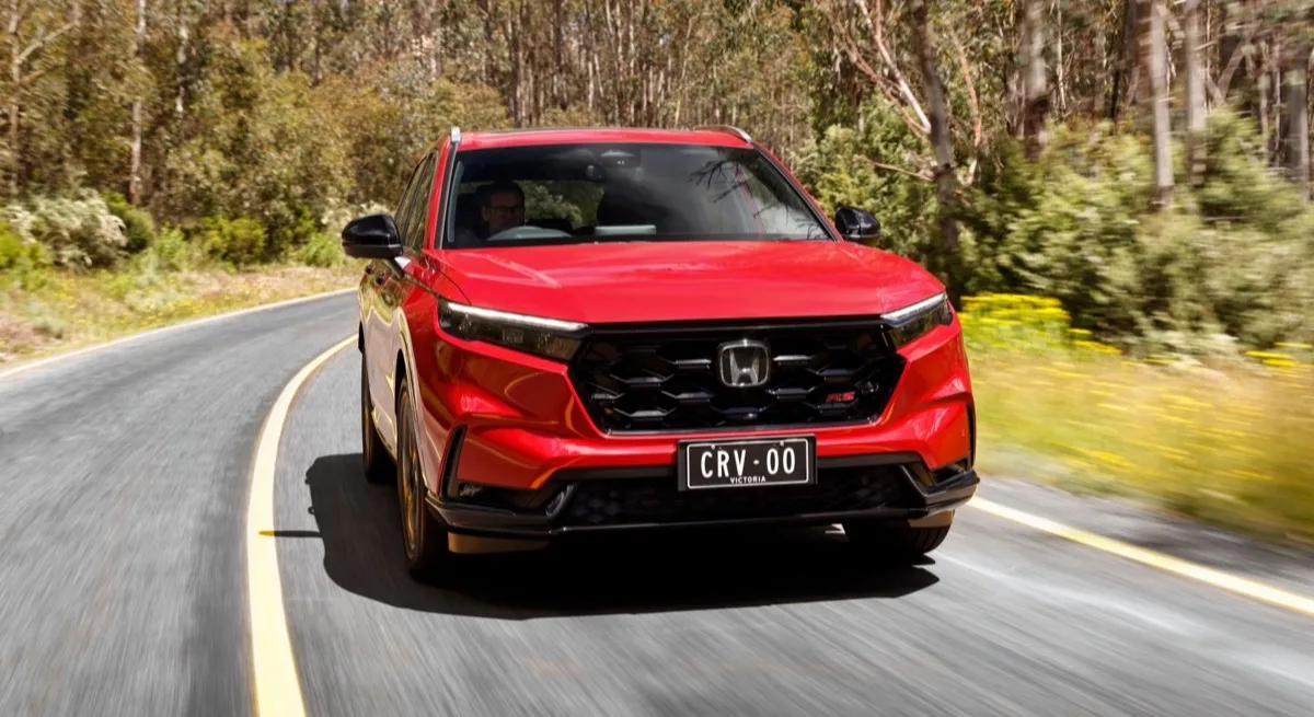 2026 Honda CR-V e:HEV hybrid in red front view driving on tree-lined road