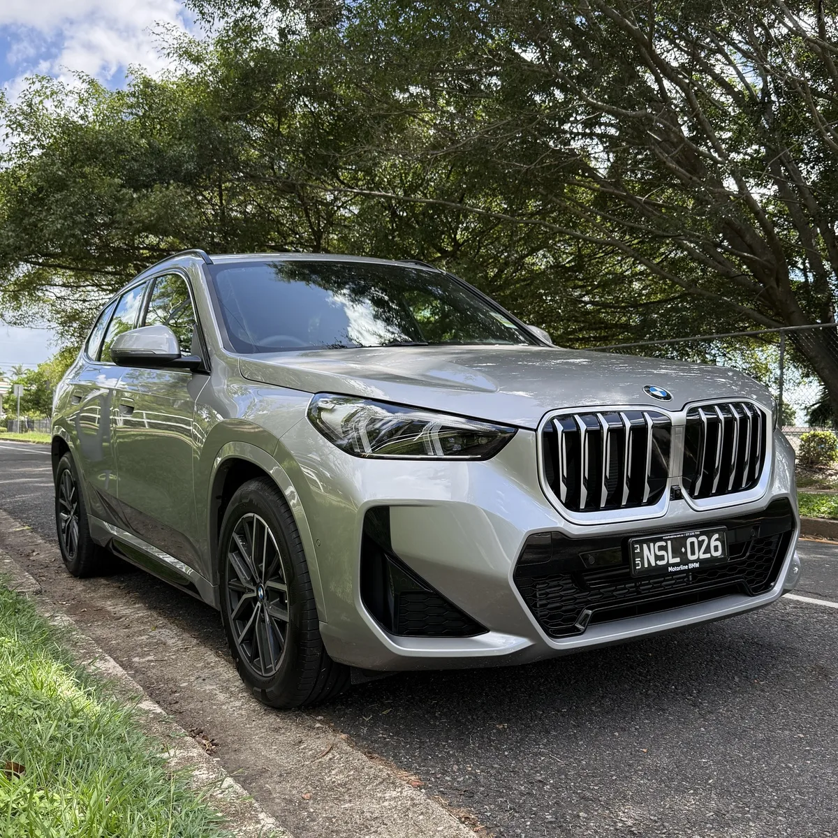 BMW X1 front three-quarter view in grey on tree-lined street