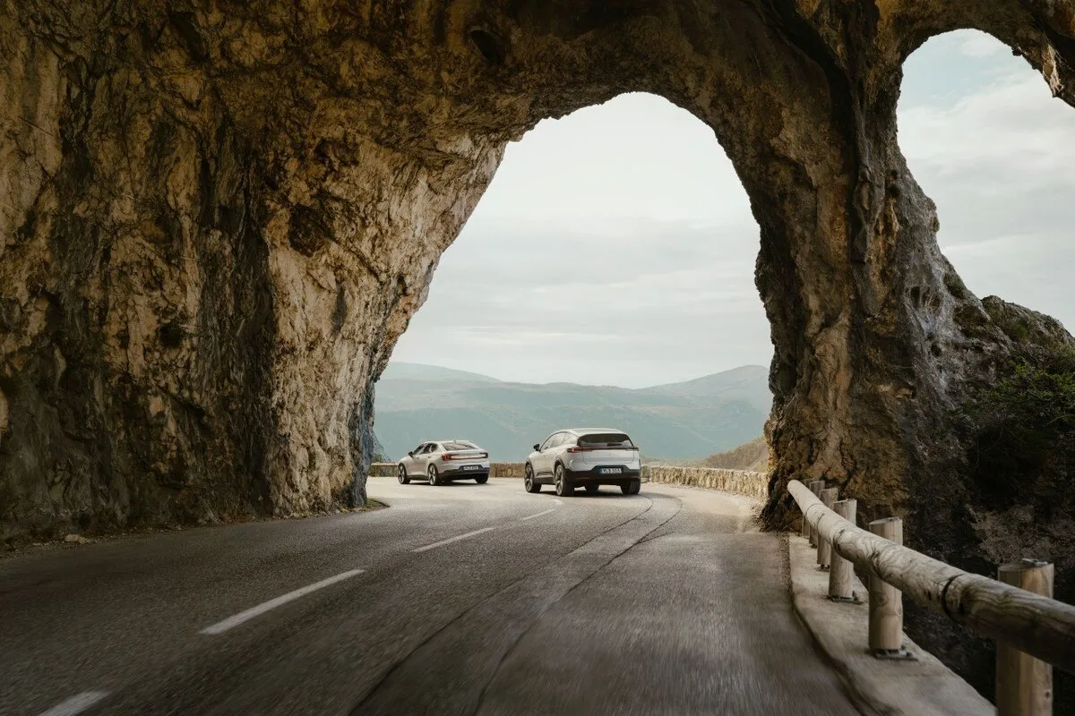 Polestar 2 and Polestar 3 driving through a natural rock arch on a mountain road