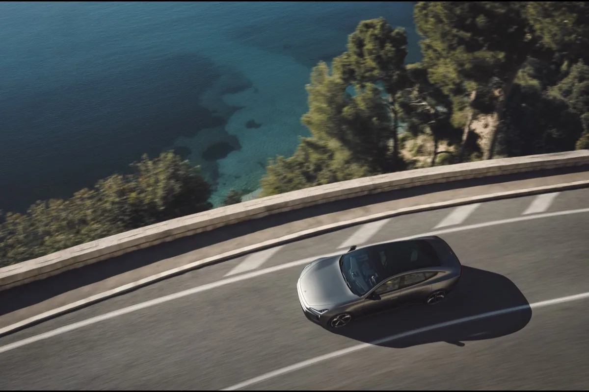 Polestar 5 aerial view driving along coastal cliff road beside turquoise sea