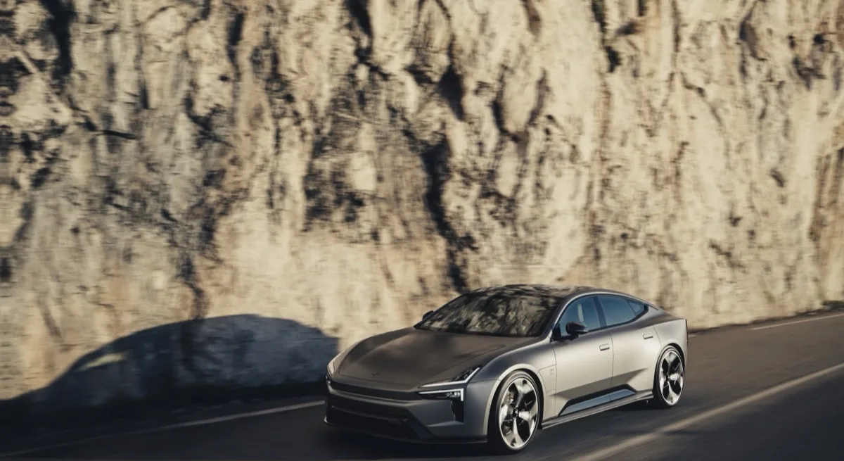Polestar 5 front three-quarter driving on coastal road with rock cliff backdrop