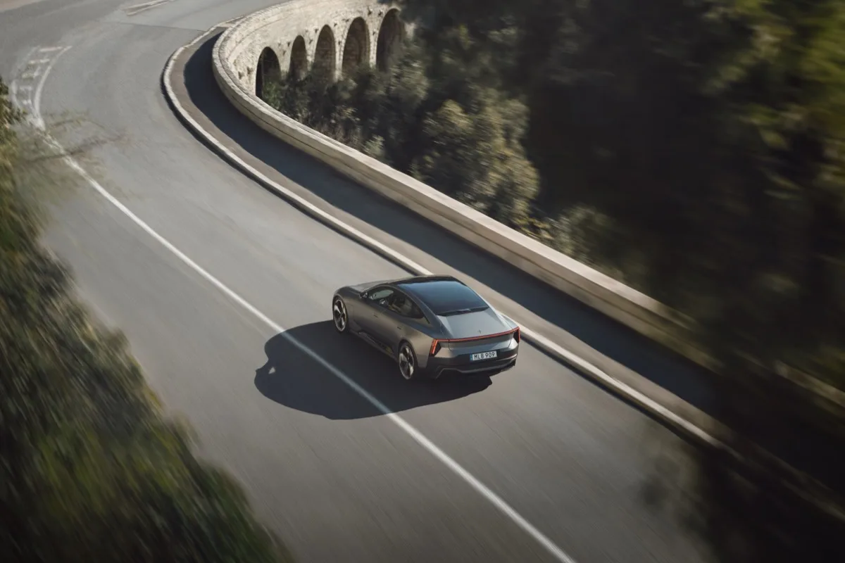 Polestar 5 in motion on winding hillside road with stone viaduct in background