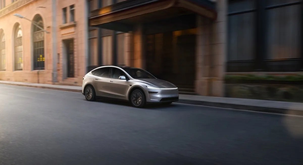 Tesla Model Y L six-seat in Cosmic Silver front three-quarter view driving past classical building