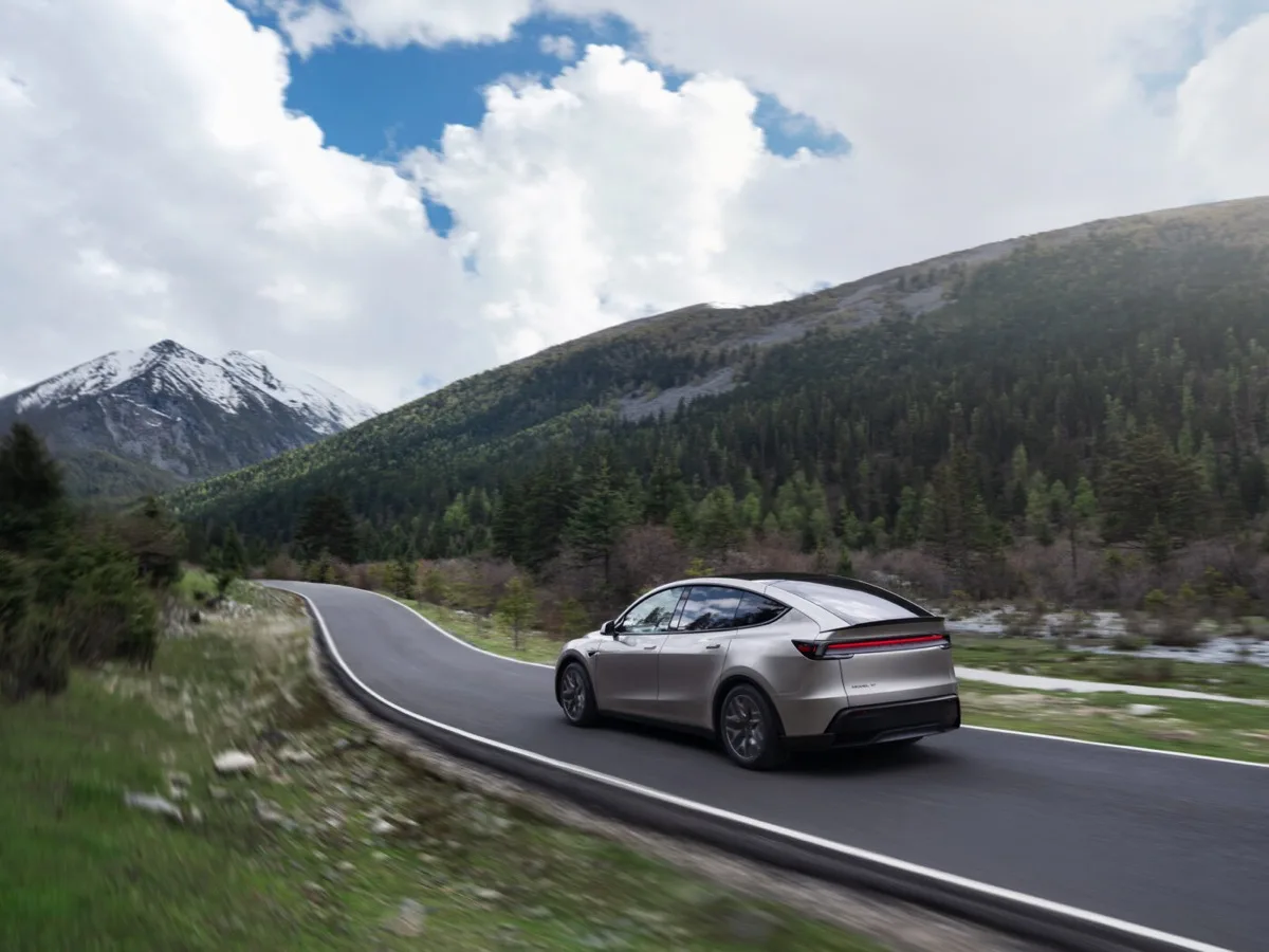 Tesla Model Y L rear three-quarter driving on mountain road with snow-capped peaks