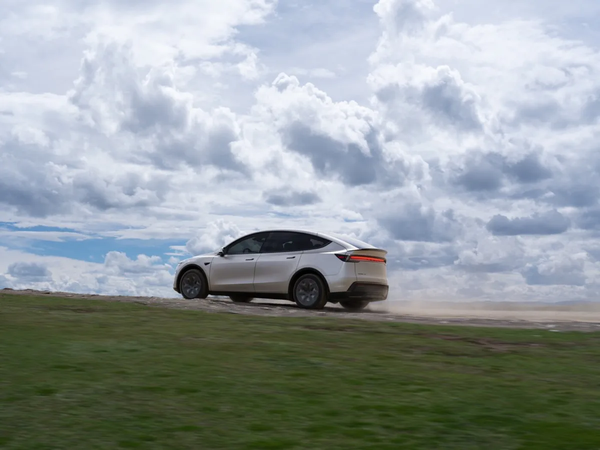 Tesla Model Y L driving on gravel road kicking up dust with dramatic sky