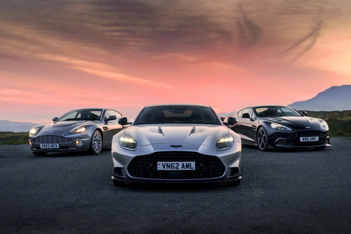 Three generations of Aston Martin Vanquish lined up at sunset with mountains in background