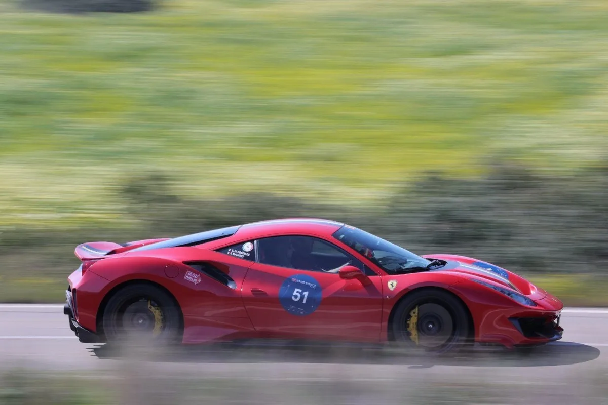Side view of a red Ferrari 488 Pista-style coupe with number 51 driving fast on a blurred country road.