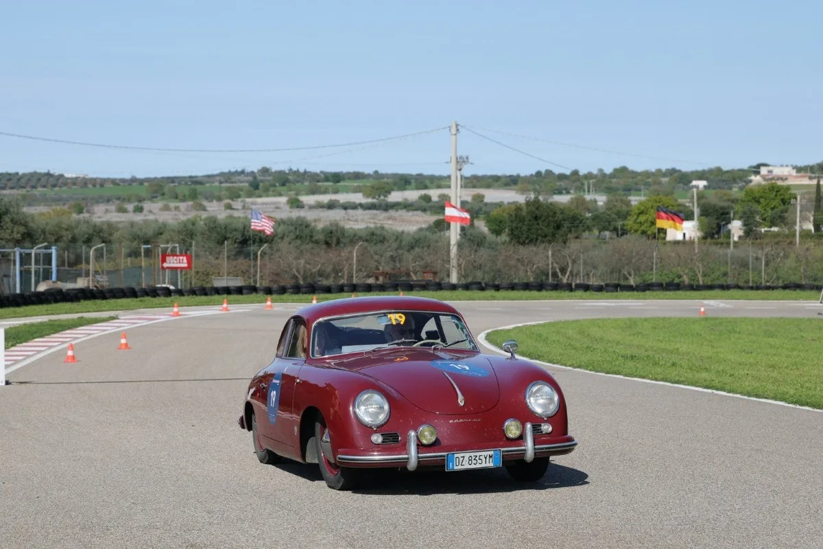 Vintage maroon Porsche 356 coupe with number 19 driving through a cone-marked racetrack turn.