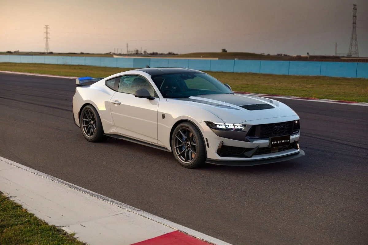 White Ford Mustang Dark Horse T8-Spec photographed from the front-left on a racetrack at sunset.