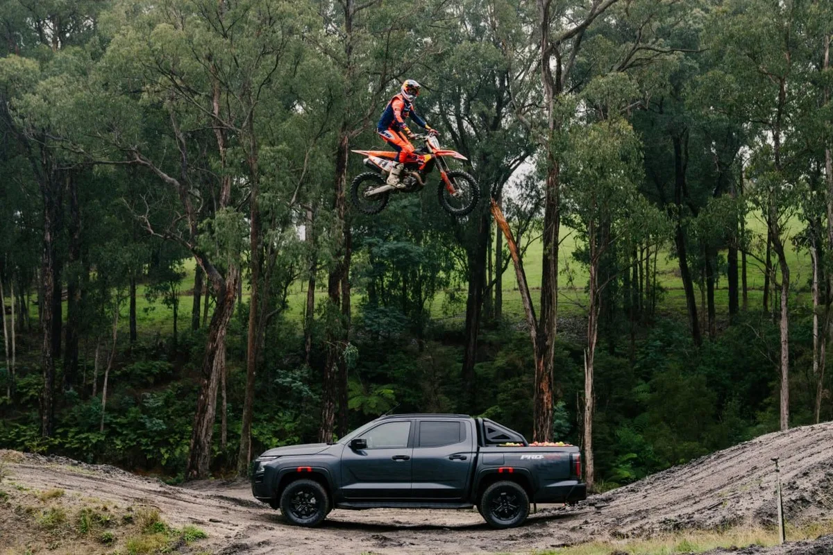 Nissan Navara PRO-4X parked beneath Daniel Sanders mid-jump in a forest riding area