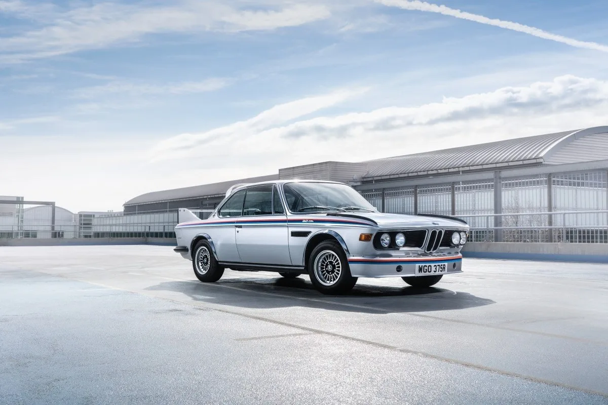 Silver BMW 3.0 CSL classic coupe with BMW Motorsport striping parked outside a modern building