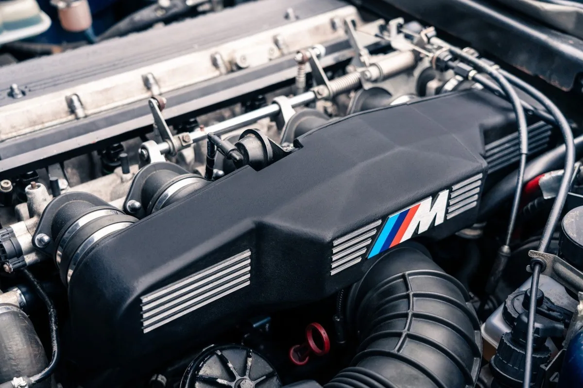Close-up of a BMW M engine cover and intake components in a classic engine bay