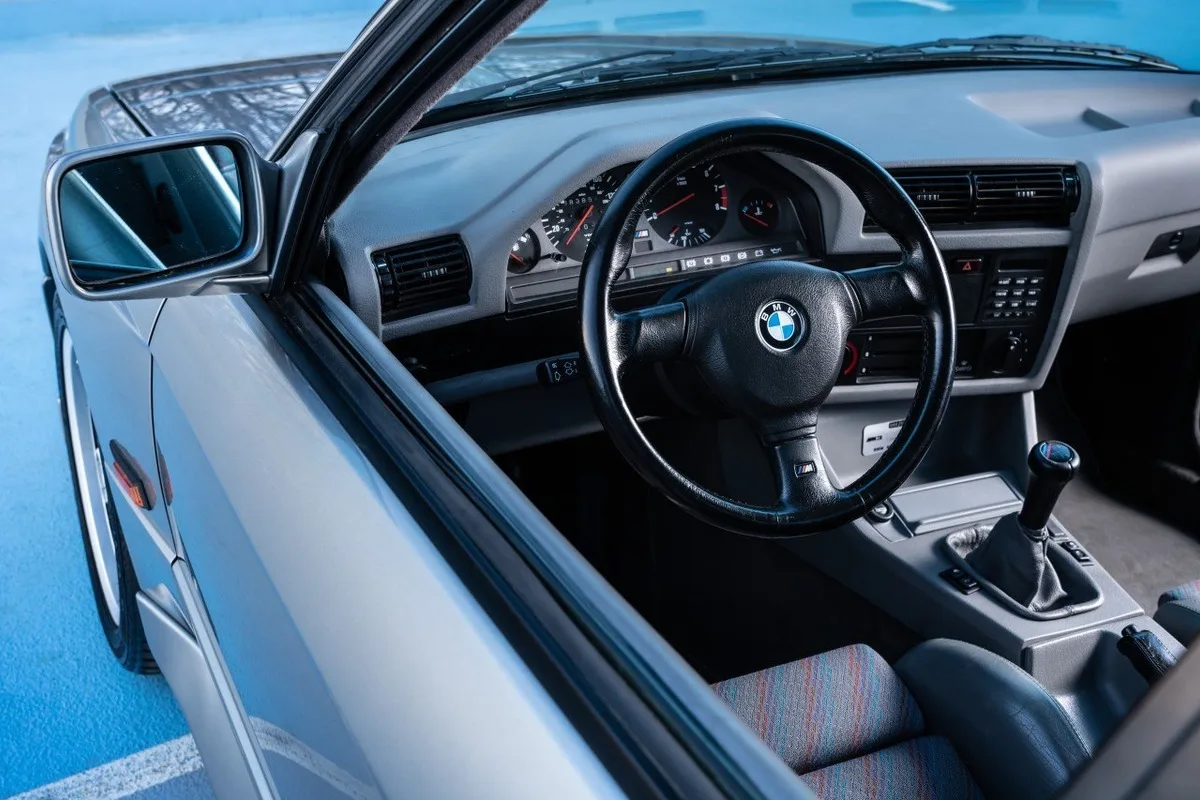 Classic BMW manual cockpit with three-spoke steering wheel, analogue gauges, and patterned sport seat