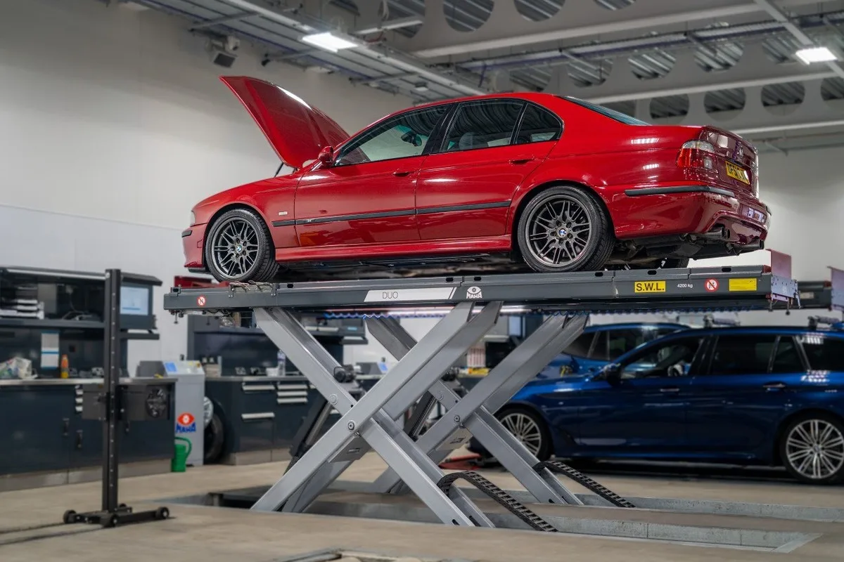 Red classic BMW sedan raised on a workshop scissor lift for service work