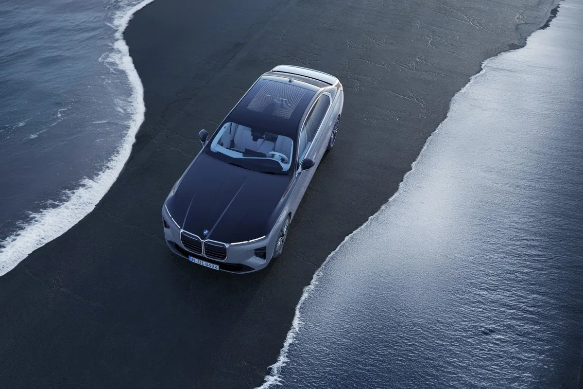 Silver BMW luxury sedan viewed from above on a black-sand beach with water and white surf on both sides.