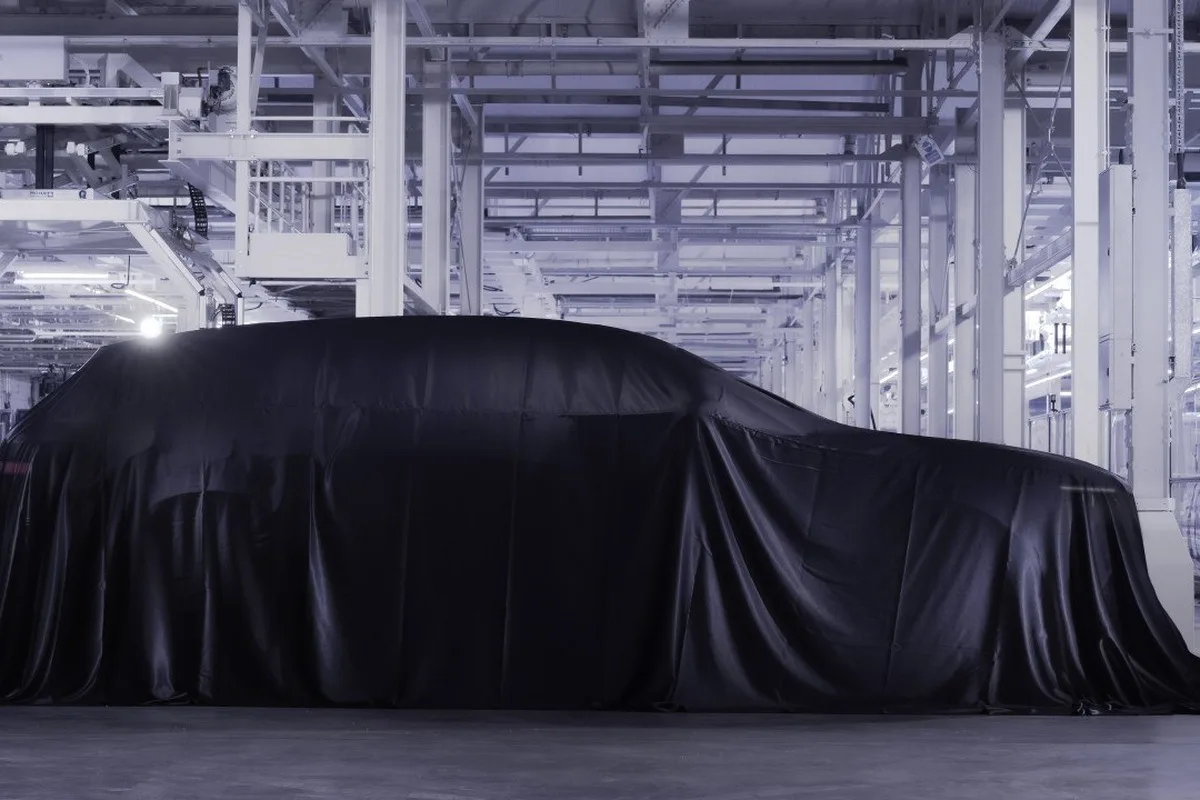 A large vehicle sits under a black cover in a bright Bentley factory or assembly facility.