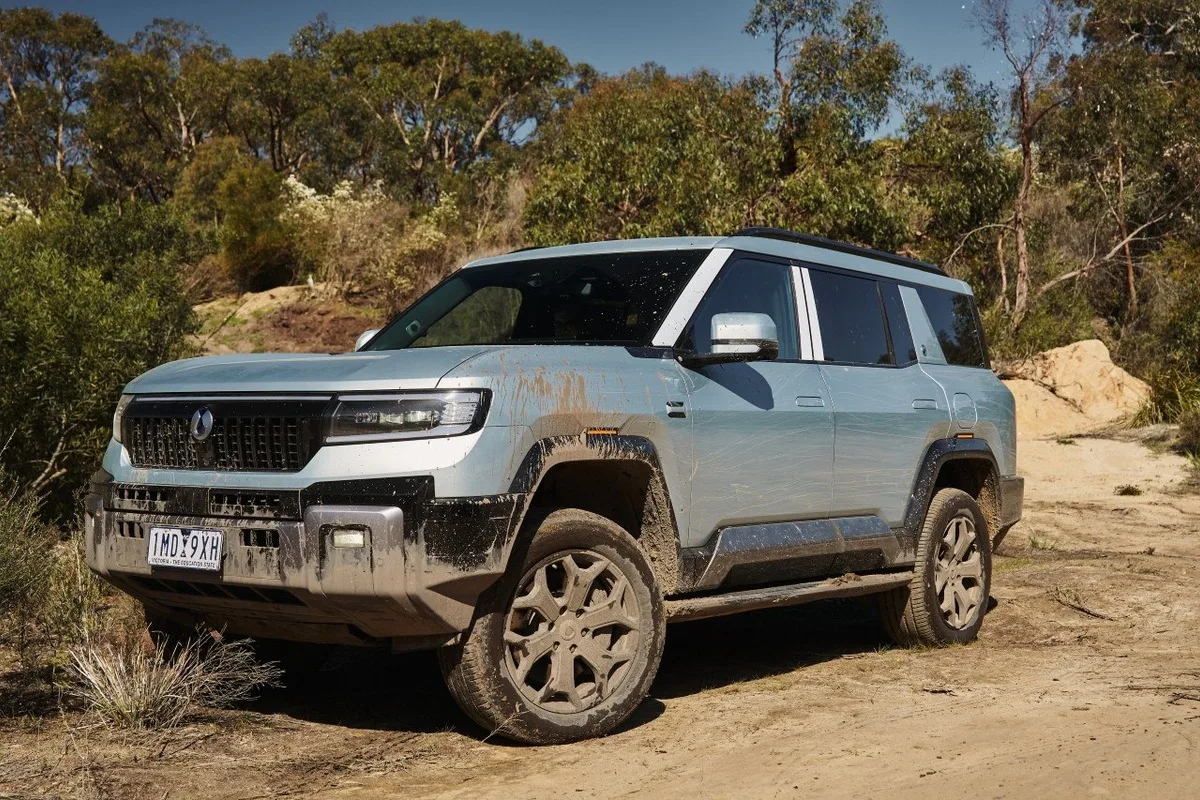 Denza B8 front three-quarter view on a dirt track with mud splashed across the body