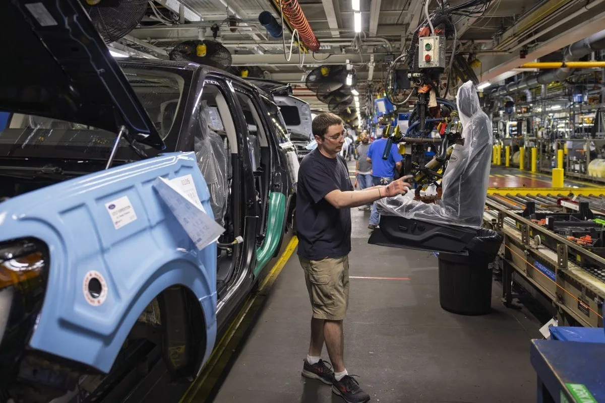 Ford assembly line worker beside a partially built vehicle at a U.S. plant.