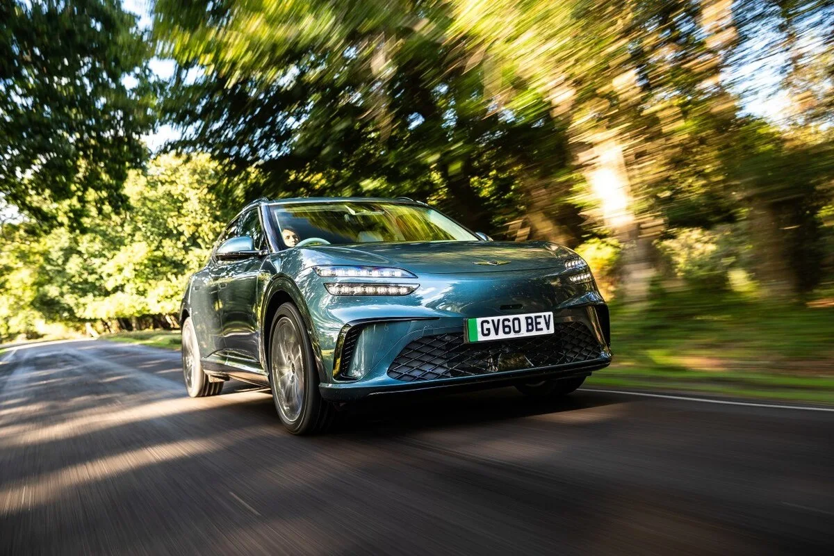 Blue Genesis GV60 electric SUV driving on a tree lined road