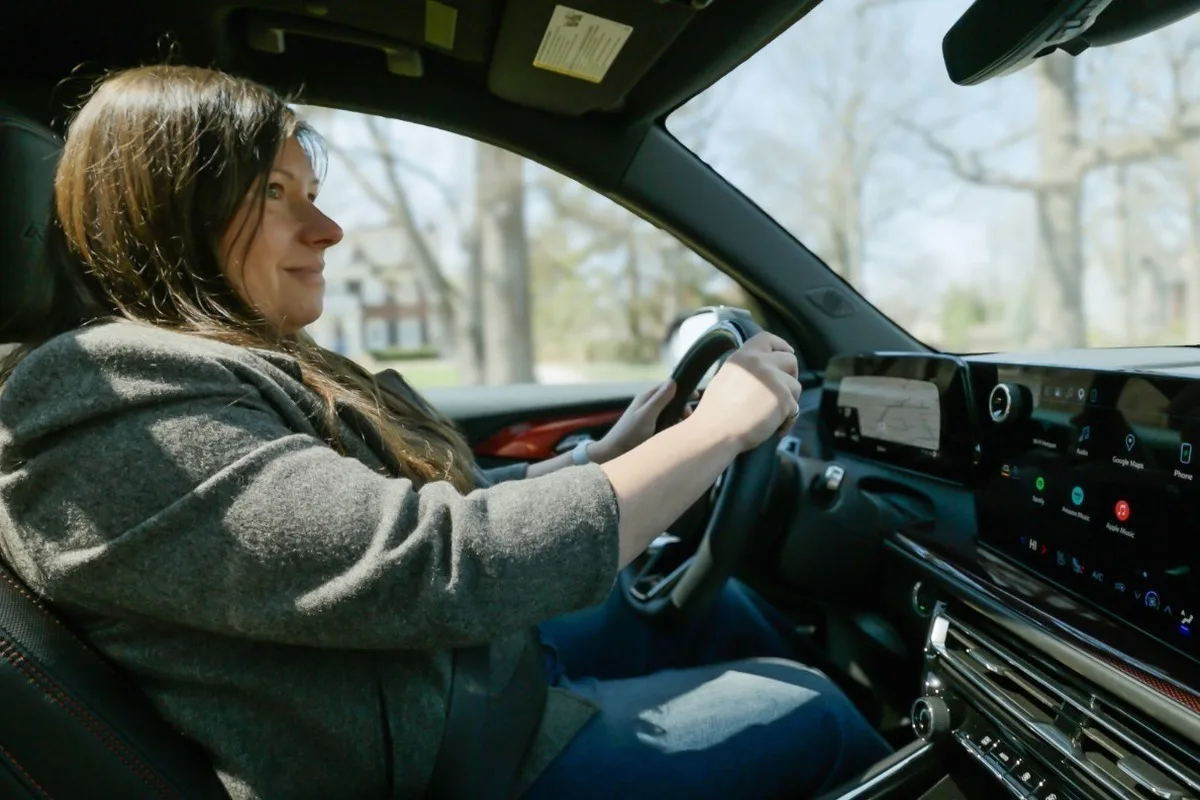 Driver in a modern GM vehicle with a wide digital dashboard and infotainment screen visible from the passenger side
