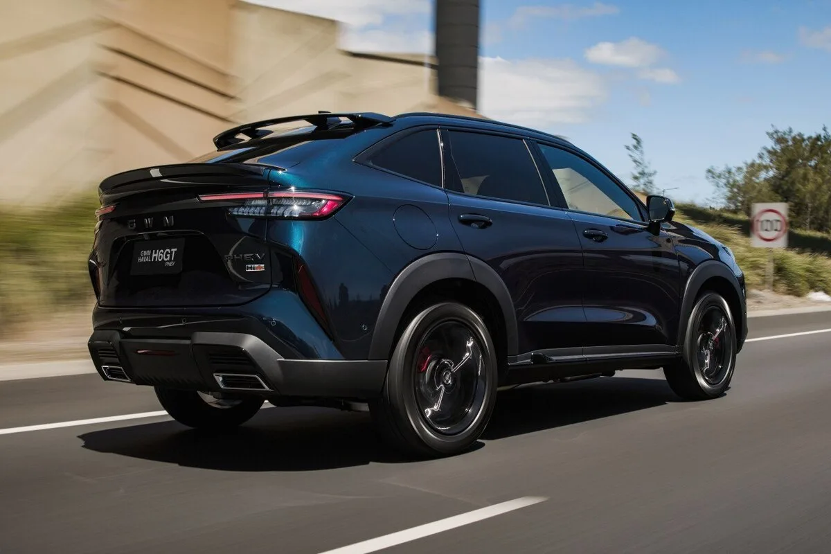 Dark blue GWM H6GT PHEV SUV driving on a road, shown from the rear three-quarter left angle