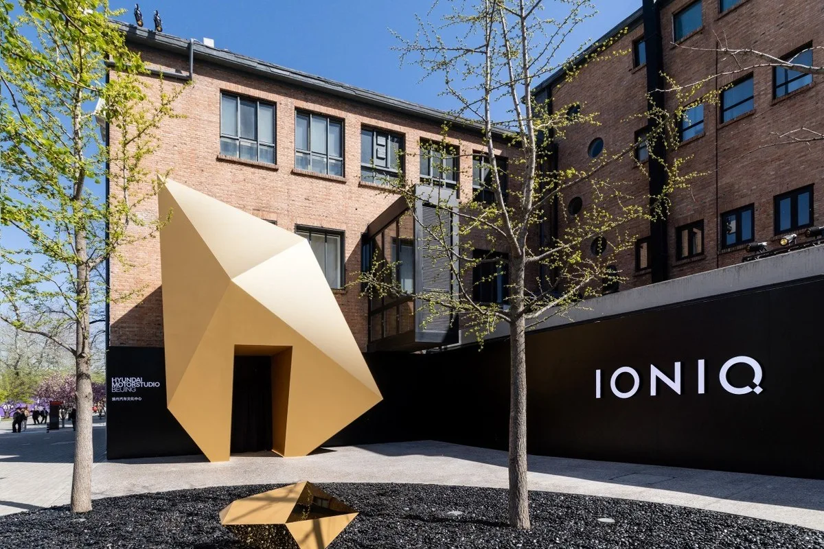 Exterior of Hyundai Motorstudio Beijing with gold geometric entrance sculpture and IONIQ branding on a black wall