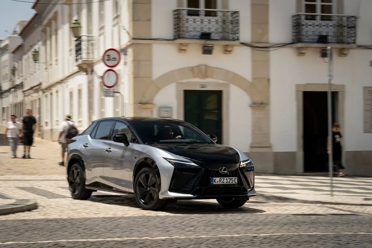 Silver and black Lexus RZ shown from the front three-quarter angle driving on a cobblestone city street.