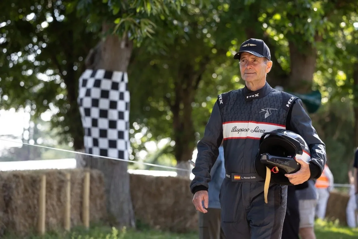 Luis Pérez-Sala walking at a motorsport event in a Hispano Suiza racing suit while carrying a helmet