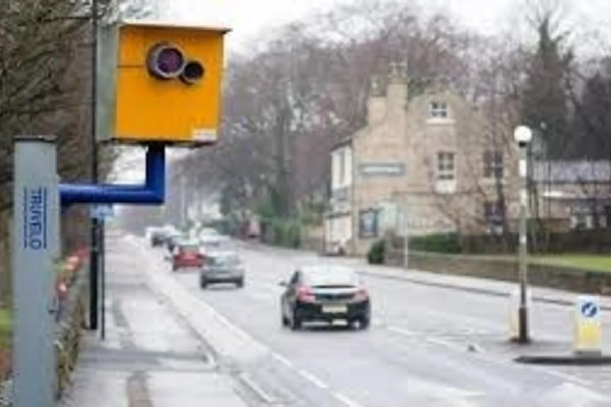 Yellow roadside speed camera mounted on a blue arm above a wet suburban street in the UK