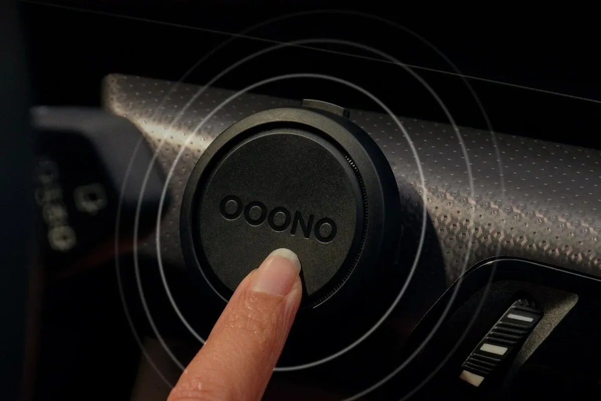 Finger pressing an OOONO device inside a car with icons for speed cameras, road hazards, and speed limits