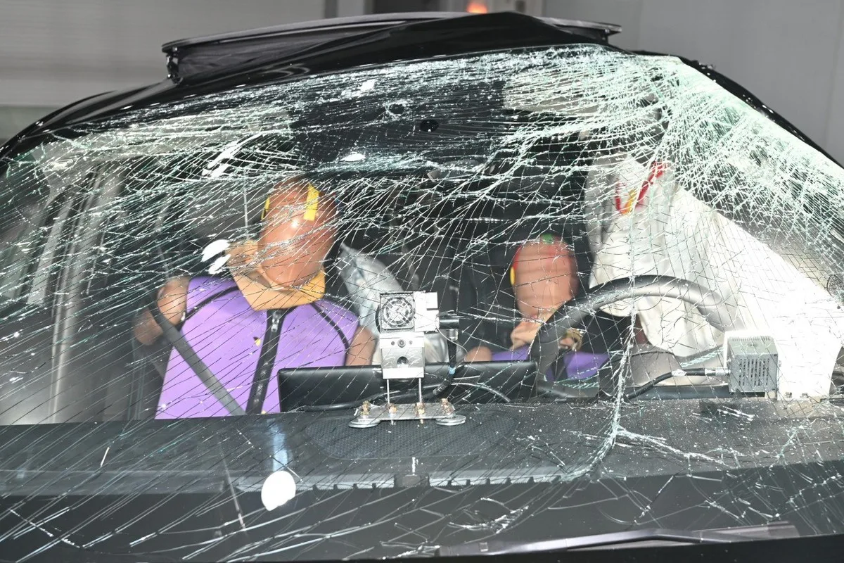Crash-test dummies and a deployed airbag behind a fractured windshield