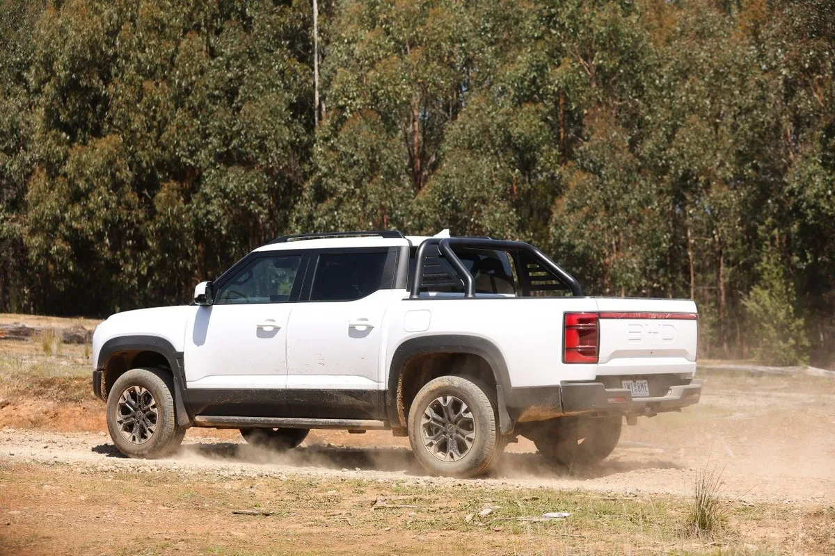 White BYD Shark 6 ute driving on a dusty dirt track, viewed from the rear.