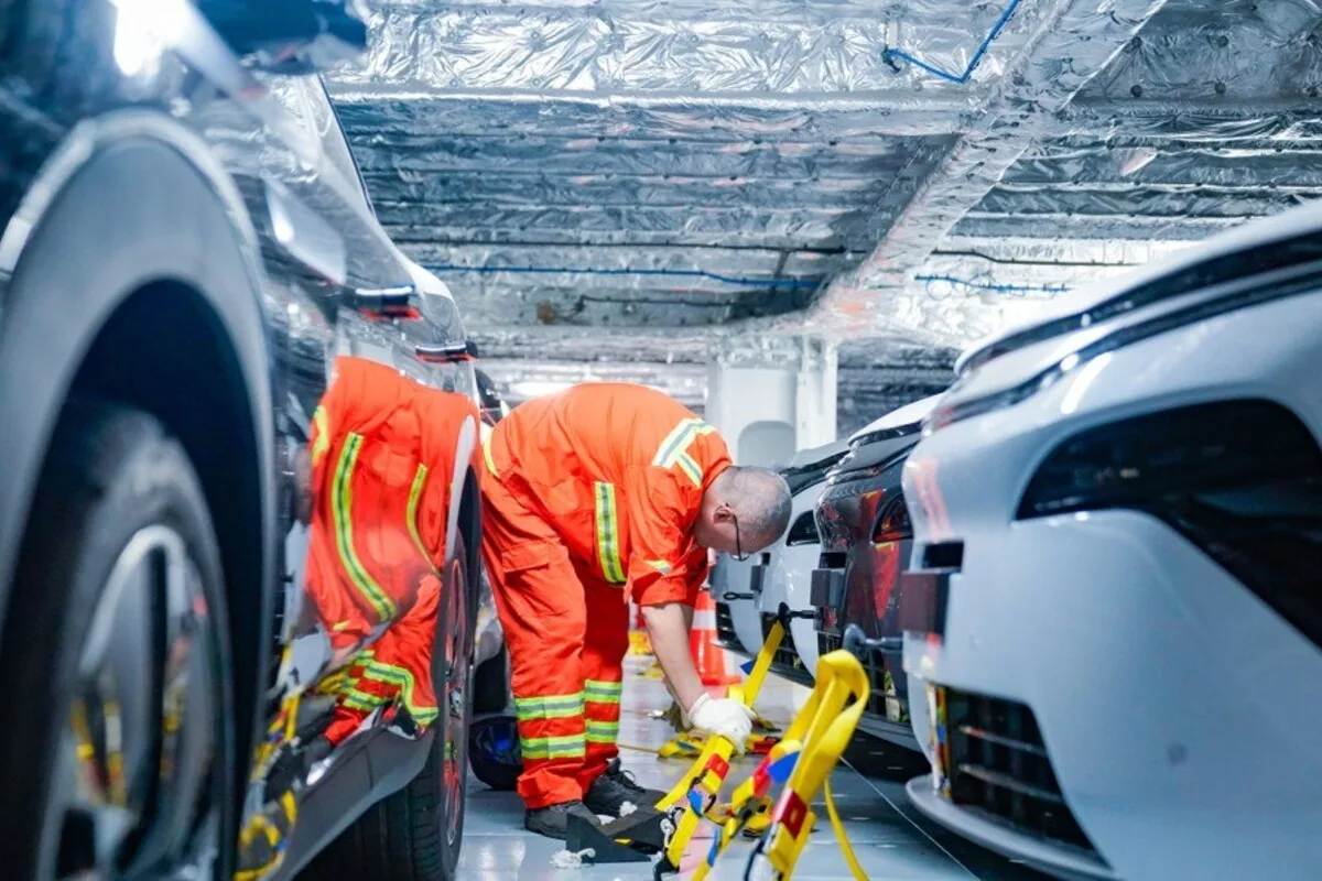 Workers in orange safety gear securing vehicles inside a BYD vehicle carrier.