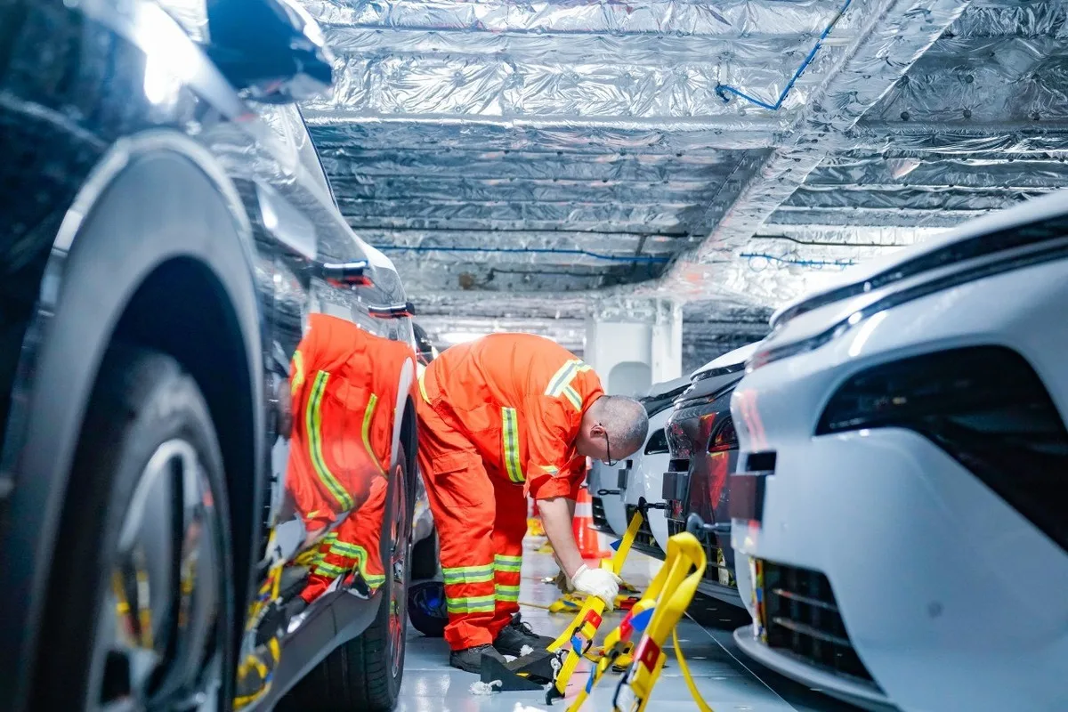 Crew member in orange coveralls securing BYD vehicles with tie-down straps inside a vehicle carrier deck