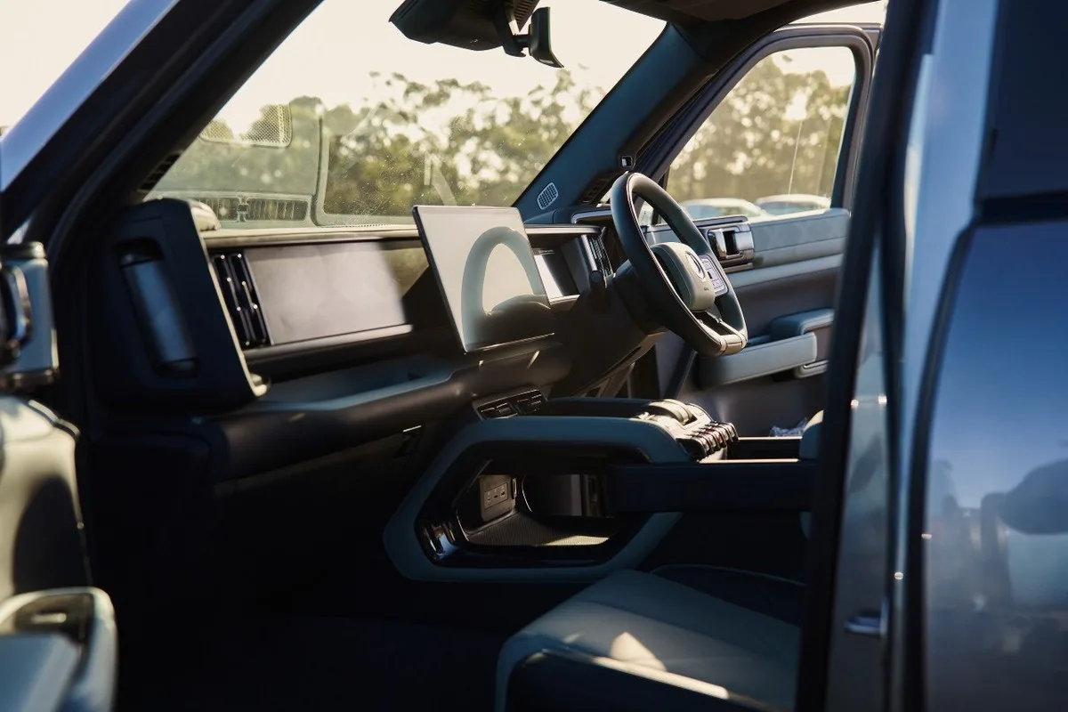 Denza B8 front cabin with central screen, console and right-hand-drive steering wheel in warm sunlight.