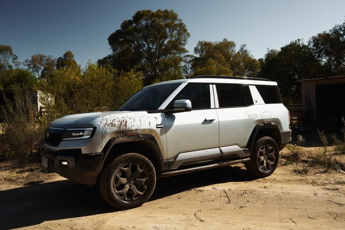 Denza B8 parked in bushland after off-road driving, with mud splashed across the front and side panels.