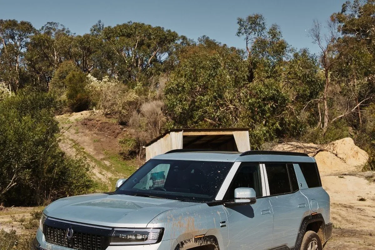 Denza B8 front three-quarter view on a dirt track, with mud on the grille, bumper and lower body.