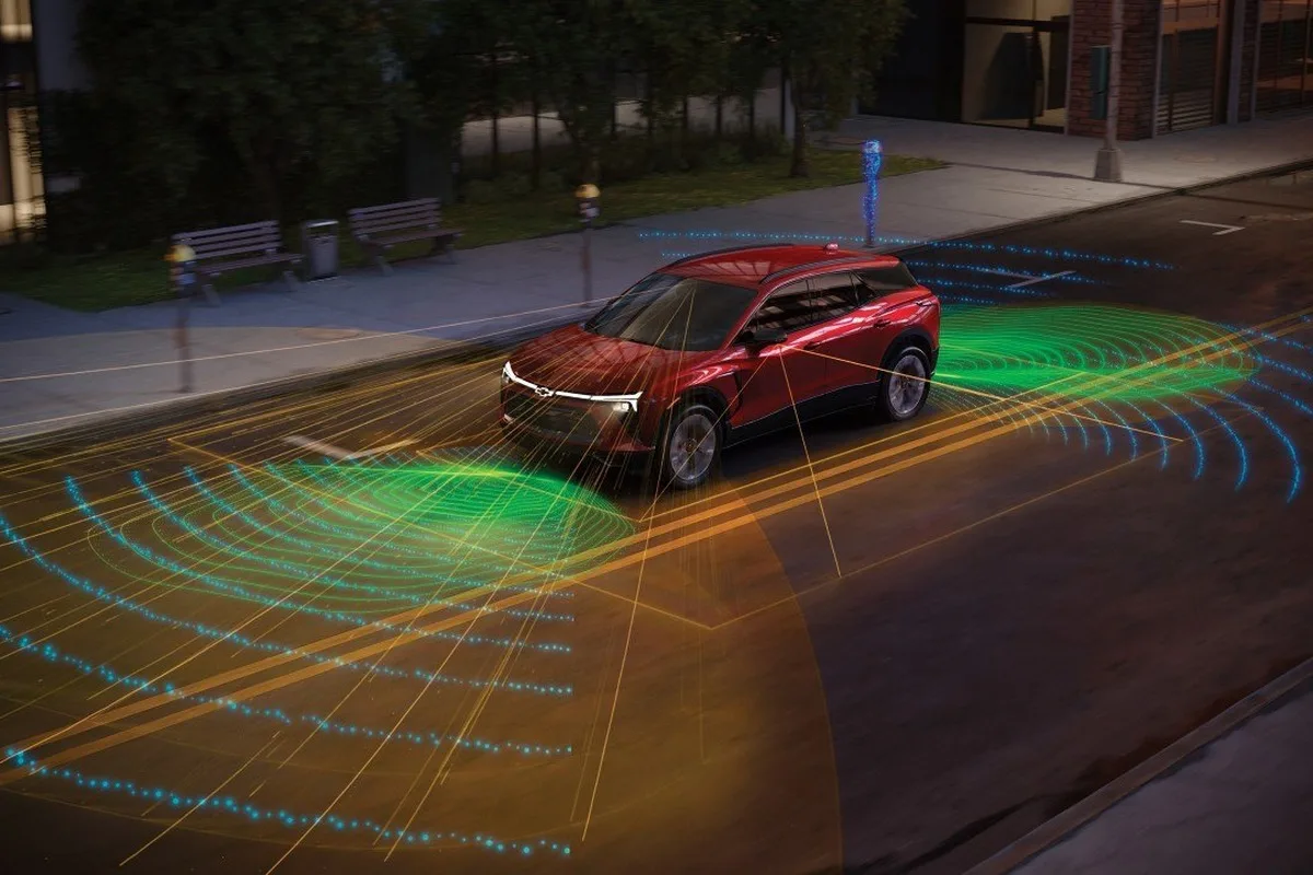 Red Chevrolet SUV driving on a city street with visualised sensor fields for driver assistance safety technology.