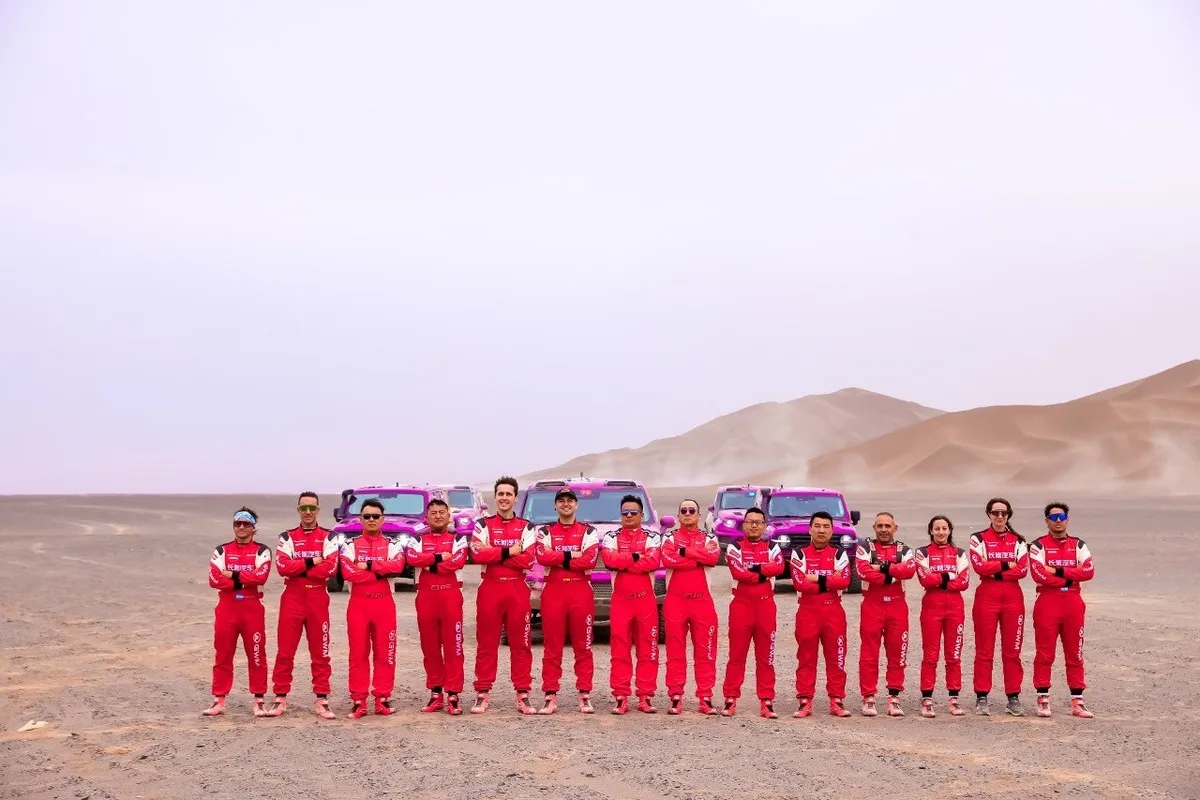 GWM factory rally team members standing with magenta TANK rally SUVs in the desert.