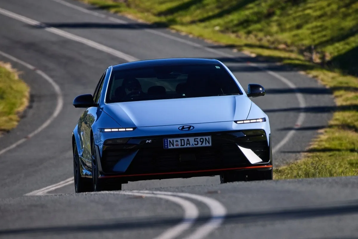 White Hyundai IONIQ 6 N driving toward the camera on a winding rural road