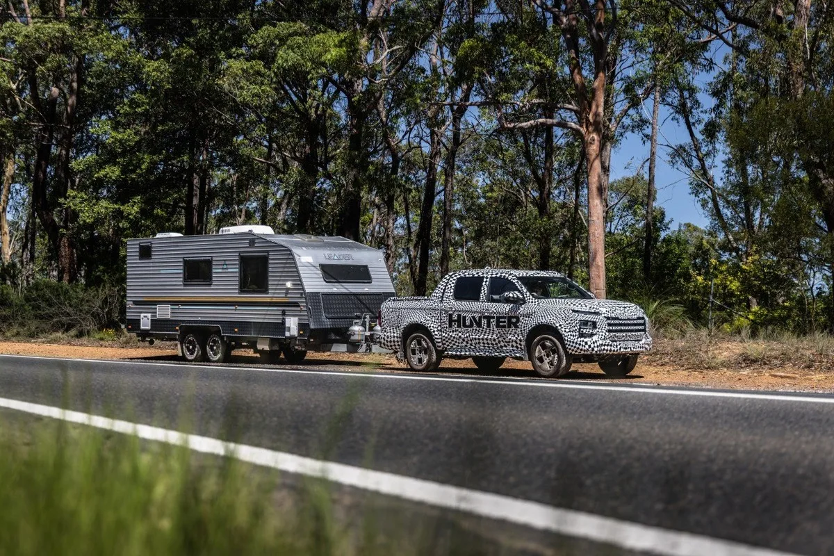 Camouflaged JAC Hunter test ute towing a caravan on an Australian road.