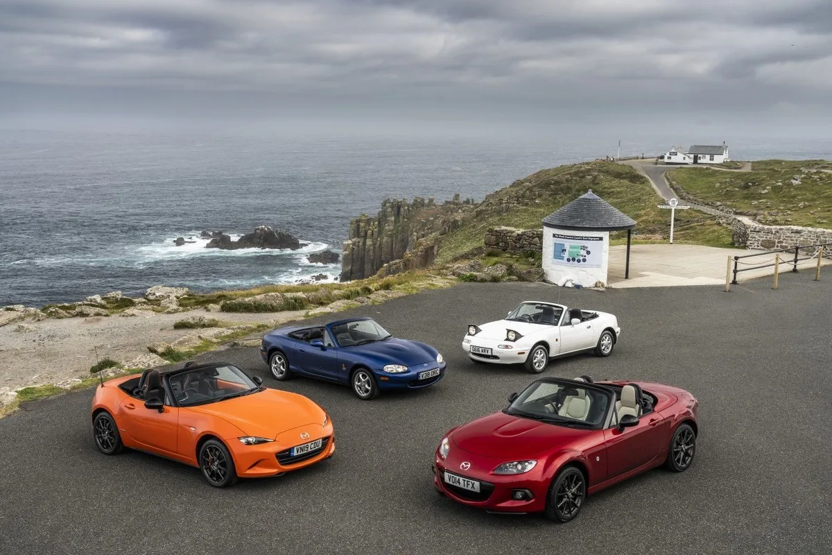 Four Mazda MX-5 roadsters parked at a coastal viewpoint during a SUSTAIN fuel heritage drive