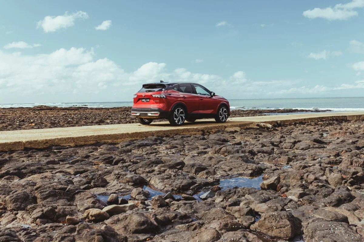 Red Nissan Qashqai e-POWER parked beside a rocky Tasmanian shoreline.