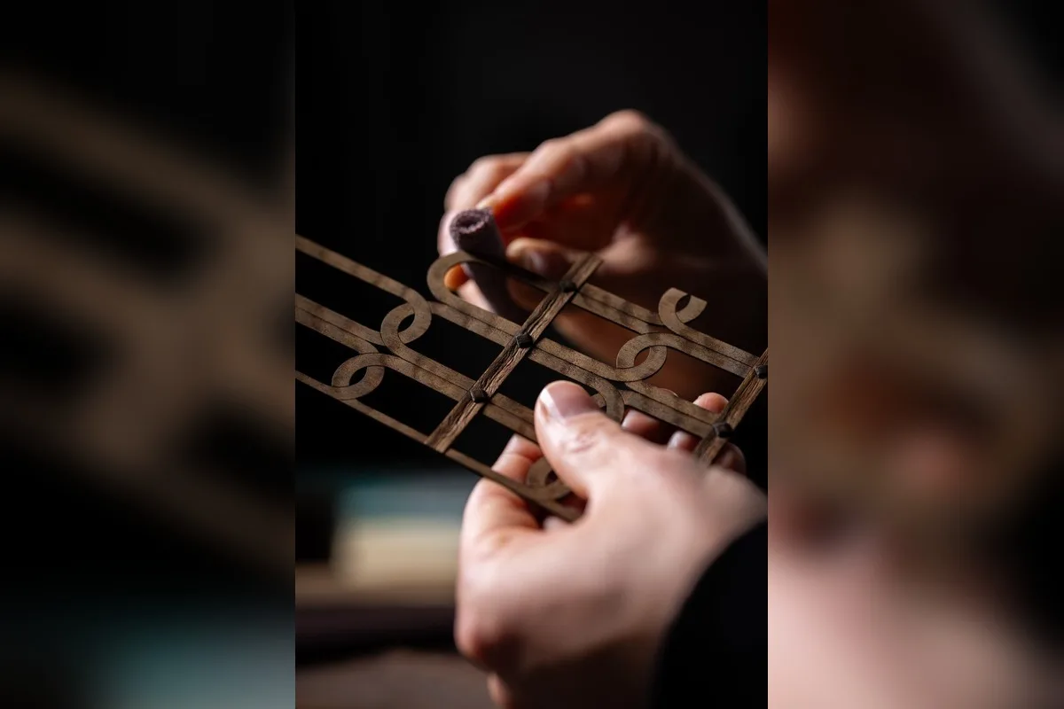 Hands working on intricate Rolls-Royce Bespoke wooden inlay with decorative scrollwork.